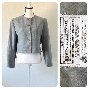 Könnte beinhalten: Ein grauer, kurzer Blazer mit Knopfleiste und einem Etikett mit der Aufschrift "Miss Pendleton, Trademark Reg. U.S. Pat. Off., Pendleton Woolen Mills, Portland, Oregon, 100% Virgin Wool, Pure Virgin Wool, Made in U.S.A."