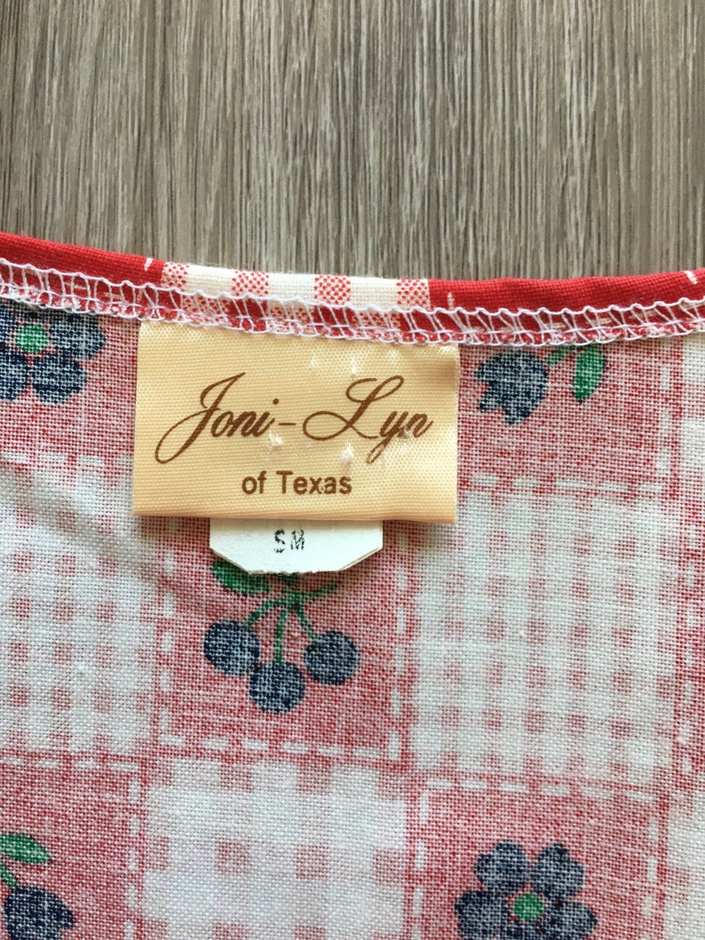 May include: A close-up of a white and red gingham fabric with a brown tag that reads "Joni-Lyn of Texas" and a white tag that reads "S M".