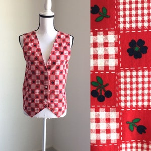 May include: A red sleeveless vest with a checkered and floral pattern. The vest has a V-neck and buttons down the front.