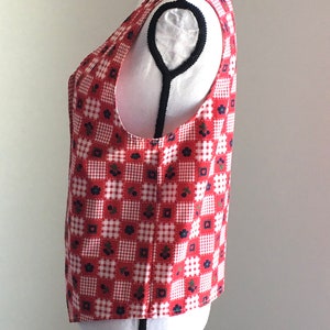 May include: A red and white gingham sleeveless vest with a floral pattern. The vest is on a white mannequin.