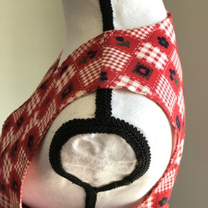 May include: Red and white gingham sleeveless dress with a black trim around the neckline. The dress has a floral pattern with small blue flowers.