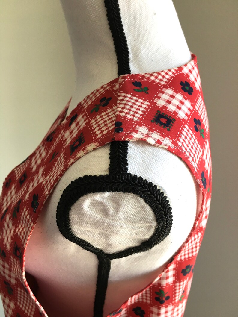 May include: Red and white gingham sleeveless dress with a black trim around the neckline. The dress has a floral pattern with small blue flowers.