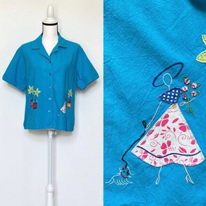 Peut inclure: Une chemise boutonnée à manches courtes bleu turquoise avec des fleurs et des plantes en pot brodées. La chemise présente un motif fantaisiste d'une femme promenant un chien.
