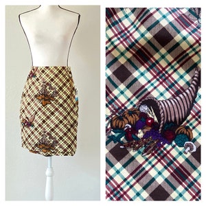 Puede incluir: Una falda de cuadros marrones y amarillos con un diseño de cornucopia que presenta una variedad de verduras y frutas de la cosecha de otoño.