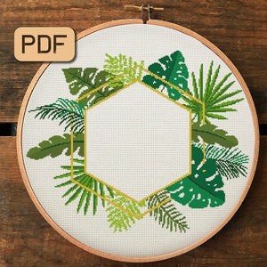 May include: A cross stitch pattern featuring a hexagonal frame with a tropical leaf design. The frame is outlined in gold thread and the leaves are in shades of green.