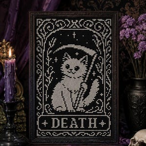 May include: A framed cross-stitch embroidery featuring a white cat holding a scythe, set against a black background. The design is enclosed in an ornate border with stars and includes the word DEATH in a rectangular banner at the bottom.