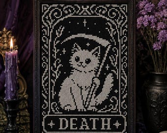 May include: A framed cross-stitch embroidery featuring a white cat holding a scythe, set against a black background. The design is enclosed in an ornate border with stars and includes the word DEATH in a rectangular banner at the bottom.