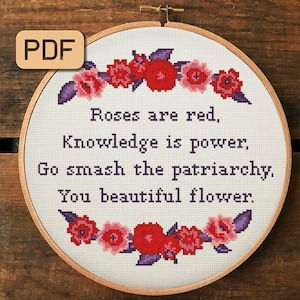 以下が含まれることがあります： 紫と赤の花柄の白い刺繍枠に「Roses are red, Knowledge is power, Go smash the patriarchy, You beautiful flower.」というテキストが書かれています。
