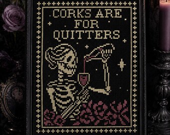 Può includere: Un ricamo a punto croce incorniciato su tessuto nero che raffigura uno scheletro che versa vino rosso in un bicchiere. Il testo CORKS ARE FOR QUITTERS è ricamato in filo color crema. Il design include piccole stelle e motivi floreali rossi.