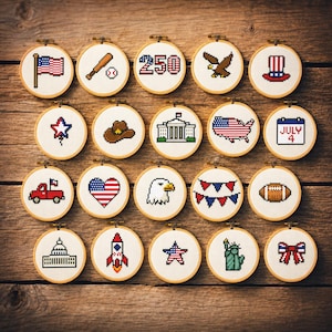 May include: A collection of twenty circular wooden embroidery hoops, each containing a unique pixel art cross-stitch design featuring American-themed icons like the flag, a bald eagle, the White House, a baseball, a rocket, and a July 4 calendar.
