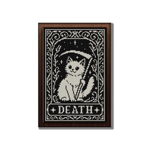 May include: A framed cross-stitch embroidery featuring a white cat holding a scythe, set against a black background with white stars and decorative borders. The word DEATH is printed in white capital letters at the bottom of the rectangular design.