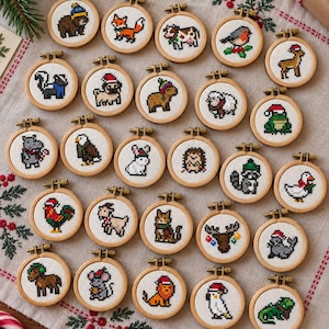 Könnte beinhalten: Eine Sammlung von fünfundzwanzig kleinen runden Holzstickrahmen, die jeweils ein einzigartiges Pixel-Art-Kreuzstichmotiv eines Tieres enthalten, darunter ein Bär, Fuchs, Kuh, Rotkehlchen, Hirsch, Stinktier, Mops, Wasserschwein, Schaf, Frosch, Nilpferd, Adler, Kaninchen, Igel, Waschbär, Ente, Hahn, Ziege, Katze, Elch, Robbe, Maus, Löwe, Kakadu und eine Eidechse.