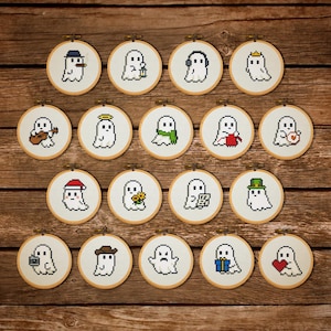 May include: Eighteen cross-stitch embroidery hoops, each with a pixelated ghost design. The ghosts are depicted in various outfits and with accessories, including hats, headphones, and gifts. The hoops are arranged on a wooden background.