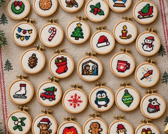 May include: A collection of twenty-eight small circular wooden embroidery hoops, each featuring a unique pixel-art style cross-stitch design related to Christmas and winter themes, including a snowman, reindeer, gifts, and holiday greenery.
