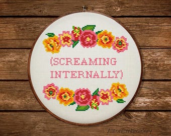 Könnte beinhalten: Ein weißer Stickrahmen mit einem rosa und gelben Blumendesign am Rand. Der Text "(SCREAMING INTERNALLY)" ist in der Mitte gestickt.