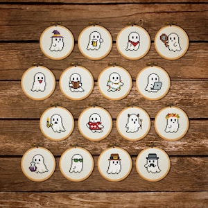 May include: A collection of small, round cross-stitch hoops featuring pixelated ghost designs. Each ghost is dressed in a unique costume or holding an item, such as a witch's hat, a book, or a detective's magnifying glass. The hoops are set against a wooden background.