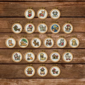 Puede incluir: Una colección de veintidós bastidores de bordado circulares de madera, cada uno con un pequeño diseño de punto de cruz en pixel art de varias razas de perros, algunos con accesorios festivos como gorros de Papá Noel o bufandas.