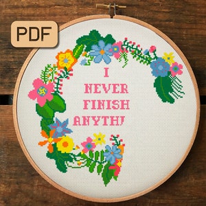 May include: Cross stitch embroidery hoop with a floral design and the text "I NEVER FINISH ANYTHING" in pink lettering.