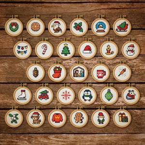 May include: A selection of small, round cross-stitch decorations with festive Christmas designs. Each decoration is set in a wooden hoop and features images such as a wreath, snowman, and Christmas tree. The decorations are arranged on a wooden surface.