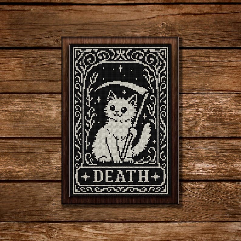 May include: A framed cross-stitch embroidery featuring a white cat holding a scythe, set against a black background with stars and floral motifs. The word DEATH is printed in white capital letters at the bottom within a decorative border.