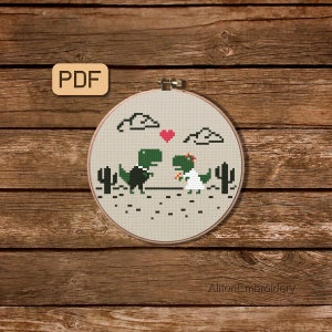 May include: Cross stitch pattern featuring a green dinosaur couple in a wedding setting. The groom dinosaur wears a black tuxedo and the bride dinosaur wears a white dress with a flower crown. The pattern includes a heart, clouds, and cacti.