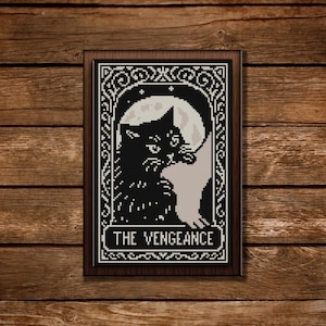 May include: A framed cross-stitch depicting a black cat against a full moon, with decorative borders and the text "THE VENGEANCE". The piece is set against a wooden backdrop, showcasing a gothic aesthetic.