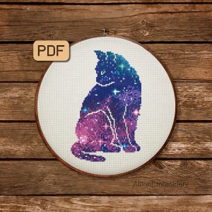 Puede incluir: Un patrón de punto de cruz de un gato con un diseño de galaxia. El gato está sentado con la cola enroscada alrededor de sus patas. El diseño de la galaxia está en tonos de morado, azul y rosa.
