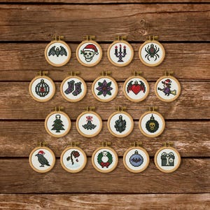 May include: A collection of nineteen small circular wooden embroidery hoops, each containing a unique cross-stitch design. The motifs include a bat, a skull with a Santa hat, a candelabra, a spider, a heart with wings, a witch, and a skull ornament.