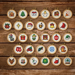 May include: A display of 28 small, circular cross-stitch embroidery hoops, each with a different Christmas design. The hoops showcase festive images like a house, Christmas tree, Santa Claus, and a reindeer, arranged on a wooden surface.
