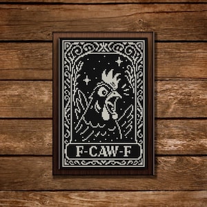 May include: Framed black and white cross-stitch art featuring a rooster with an open beak, framed by ornate scrollwork. The text "F-CAW-F" is displayed at the bottom. The artwork is set against a wooden background.