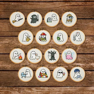 Op de afbeelding: Een verzameling van vijftien kleine, ronde kruissteekborduurringen. Elke ring toont een wit spookkarakter in verschillende kostuums en activiteiten, waaronder een ninja, een brandweerman en een fee. De ringen staan tegen een houten achtergrond.