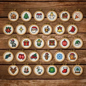 Puede incluir: Colección de pequeños aros de bordado de punto de cruz con diseños navideños. Cada aro, con marco de madera, muestra imágenes pixeladas de elementos festivos como una casa, árbol, Papá Noel y adornos, sobre un fondo de madera.