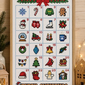 May include: A framed cross-stitch advent calendar on white fabric featuring a red bow at the top and twenty-four numbered squares containing colorful holiday icons like a snowflake, gingerbread man, snowman, and tree, with the text MERRY CHRISTMAS.