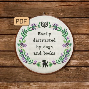 May include: A white embroidery hoop with a floral wreath design and the text "Easily distracted by dogs and books". A black silhouette of a dog is in the center of the hoop.