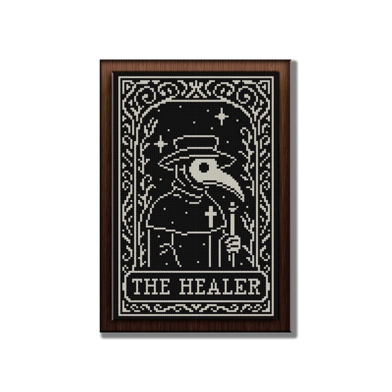 May include: A framed black and white cross-stitch design featuring a plague doctor with a long beak, hat, and cross. The text "THE HEALER" is at the bottom. The frame is a dark brown color.