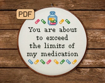 以下が含まれることがあります： 白い刺繍枠に「You are about to exceed the limits of my medication」というテキストと、カラフルな薬が詰まった小さな青い瓶が描かれています。瓶とテキストの周りにもカラフルな薬が描かれています。