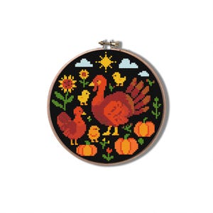 Op de afbeelding: Een kruissteek borduurring met een Thanksgiving-thema. Het ontwerp toont twee kalkoenen, zonnebloemen, pompoenen, kuikens, een zon en wolken, allemaal in tinten oranje, geel en groen tegen een zwarte achtergrond. De ring is rond met een houten frame.