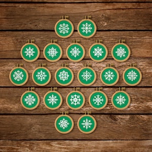 May include: A collection of small, round embroidery hoops featuring green fabric and white snowflake designs. The hoops are arranged on a wooden surface, displaying different snowflake patterns. The wooden hoops are held in place by a metal clasp.