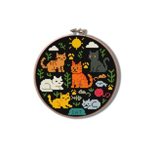 以下が含まれることがあります： 黒い背景に、オレンジ、黄色、白、グレーのピクセル化された猫が描かれたクロスステッチ刺繍枠。デザインには、太陽、雲、猫の足跡、猫の餌入れが含まれています。