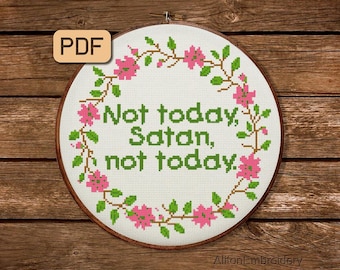 Op de afbeelding: Een witte kruissteek borduurring met een groene bloemenkrans en de tekst "Not today, Satan, not today." De ring is op een bruine houten achtergrond.