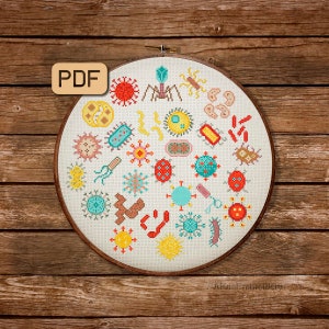 May include: A white embroidery hoop with a colourful cross-stitch design of various microbes, including bacteria, viruses, and fungi. The hoop is on a wooden background.