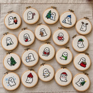 May include: A collection of twenty small circular wooden embroidery hoops, each containing white fabric with a unique cross-stitch design of a white ghost engaged in various holiday activities, including holding ornaments, trees, gifts, and wearing winter hats.