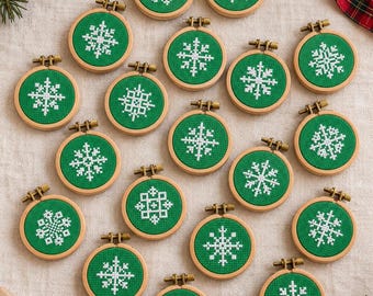 May include: A collection of small, round wooden embroidery hoops, each containing green fabric with a unique white cross-stitched snowflake pattern. Each hoop features a small metal tightening screw at the top, arranged in a scattered display.