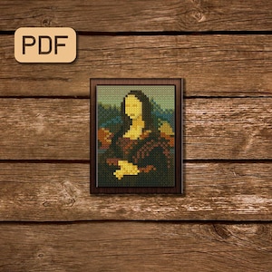 Op de afbeelding: Een ingelijst pixel art-beeld van de Mona Lisa, een beroemd schilderij van Leonardo da Vinci. Het beeld is in een bruin frame en is geplaatst tegen een houten achtergrond.