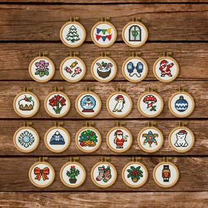 May include: A collection of twenty-five small circular wooden embroidery hoops, each containing a unique pixel art cross-stitch design featuring various holiday and winter themes, including a Christmas tree, Santa Claus, ornaments, and festive plants.