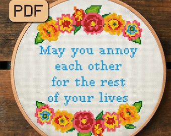 Può includere: Un cerchio da ricamo bianco con un motivo floreale blu e il testo "May you annoy each other for the rest of your lives".