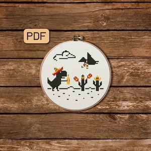 May include: Cross-stitch hoop art depicting a black dinosaur in a sombrero, holding a bottle, and near cacti. The design includes a cloud and a flying creature. The text "PDF" is in the upper left corner.