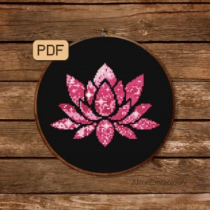 May include: A pink and white lotus flower with a sparkly design, cross-stitched on black fabric. The finished piece is displayed in a round embroidery hoop.
