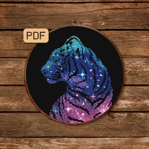 May include: A cross-stitch pattern of a purple and blue tiger with a galaxy design. The tiger is outlined in white and has a black background. The pattern is in a round embroidery hoop.