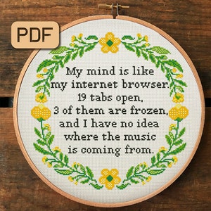 以下が含まれることがあります： 白い刺繍枠に、クロスステッチのデザインが施されています。花柄の縁取りと「My mind is like my internet browser. 19 tabs open, 3 of them are frozen, and I have no idea where the music is coming from.」というテキストが刺繍されています。